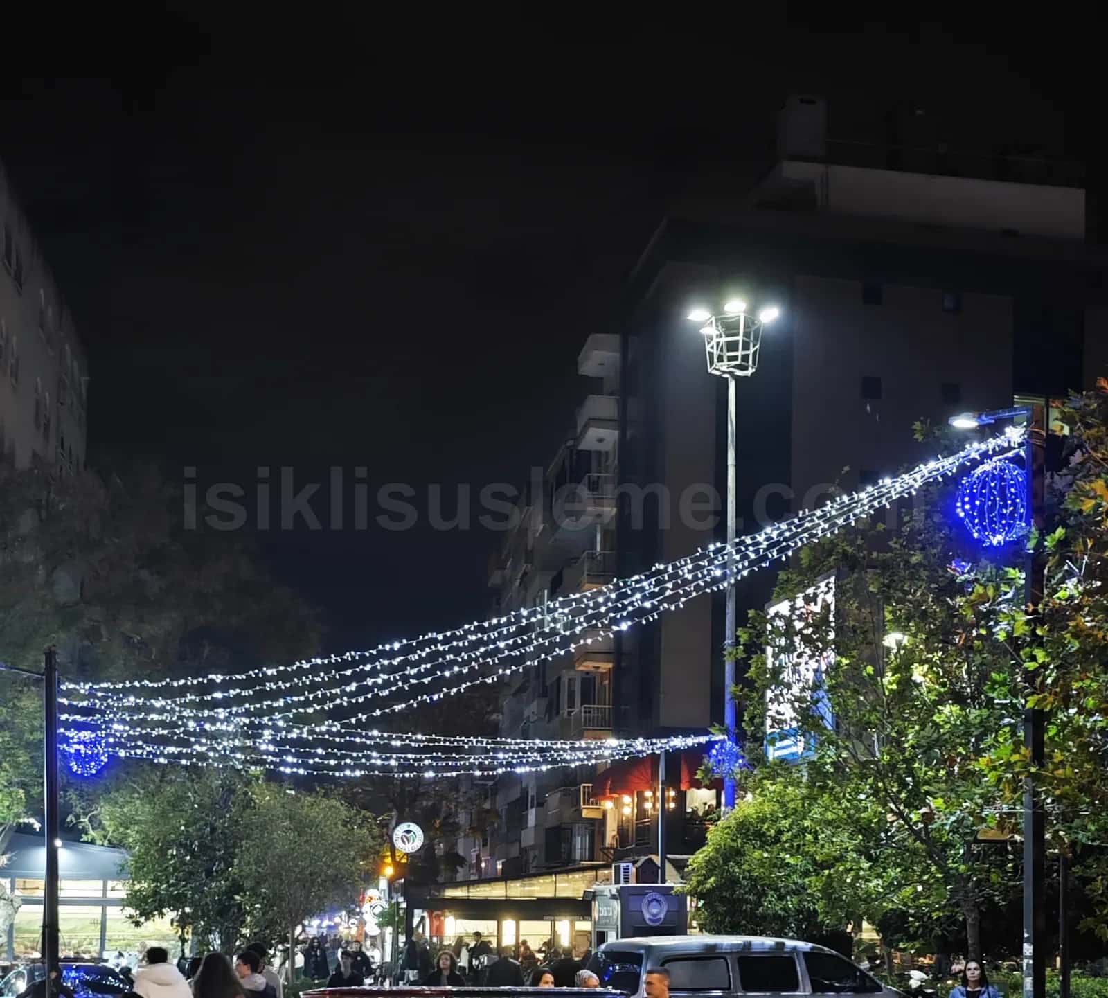 Gece sehir bulvarinda direkler arasina gerilmis mavi beyaz LED zincir susleme ve mavi LED top dekorasyonu