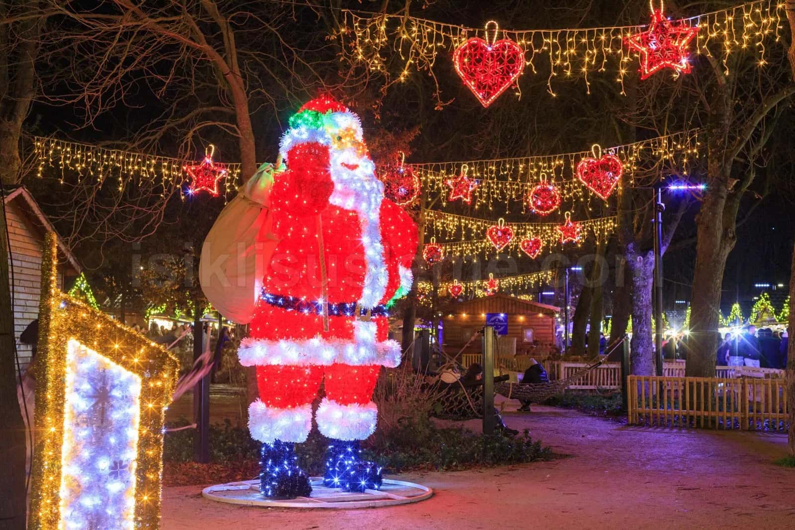 Acik alanda kirmizi noel baba LED figuru, etrafinda yildiz ve kalp motifli isik zincirleri