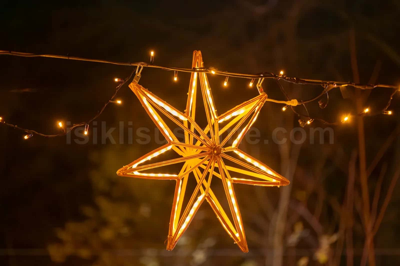 Gece dis mekanda dallara asilmis sicak sari isikli yedi kosegenli LED yildiz figuru