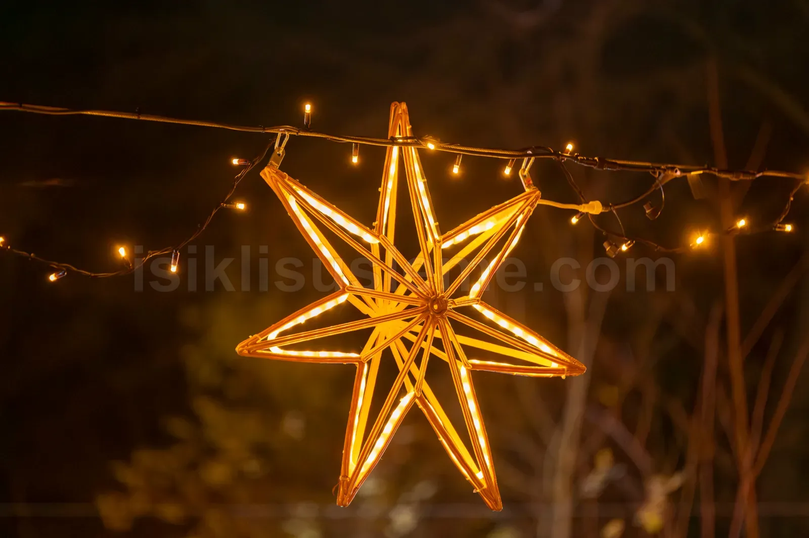 Gece dis mekanda dallara asilmis sicak sari isikli yedi kosegenli LED yildiz figuru