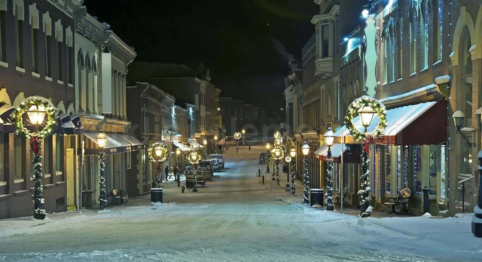 Kar yağışı altında tarihi çarşı caddesinde direk başlarına monte altın LED motifler ve mağaza girişi süslemeleri