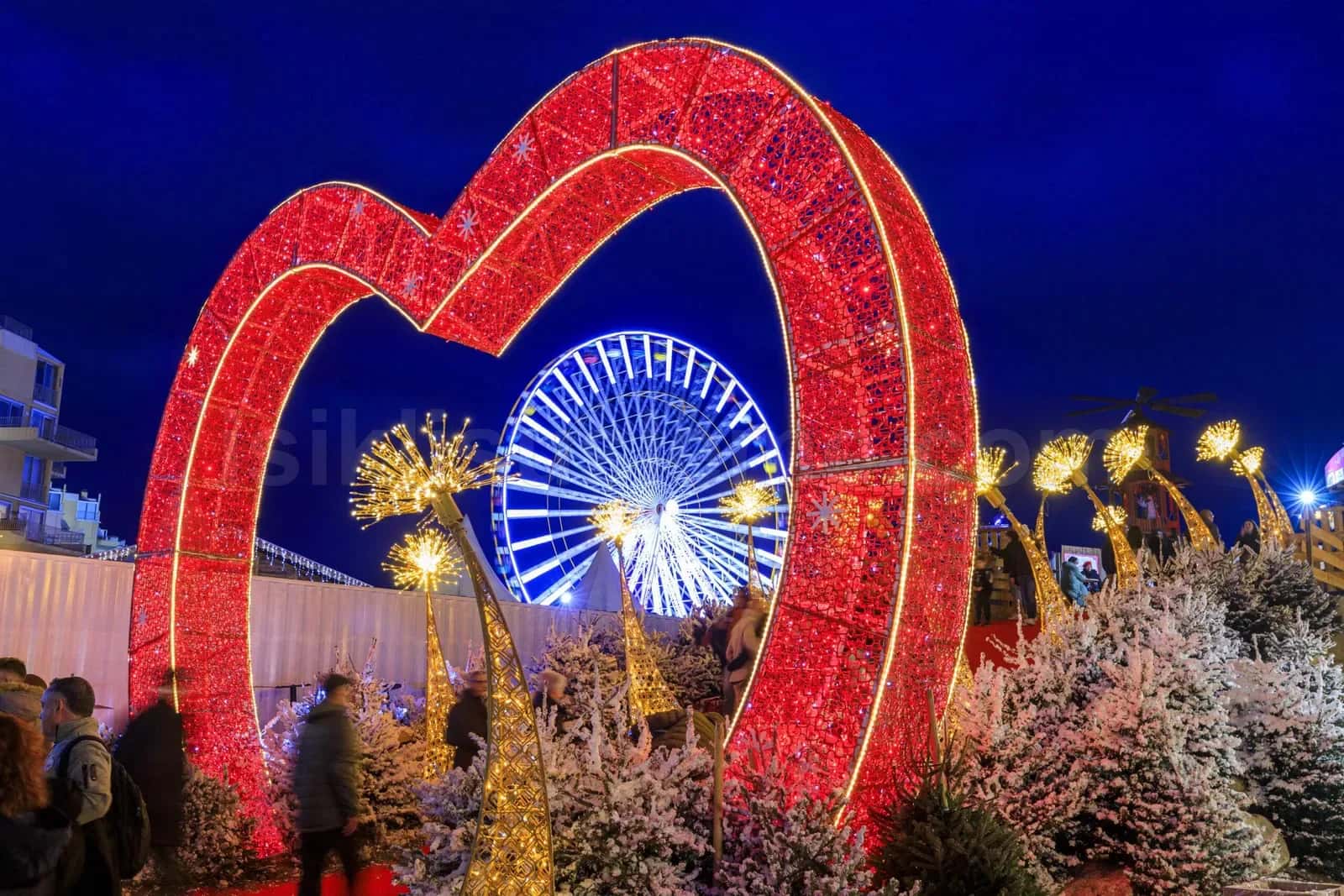 Kirmizi LED kalp kemer figuru onunde insanlar geciyor arka planda mavi aydinlatmali donme dolap