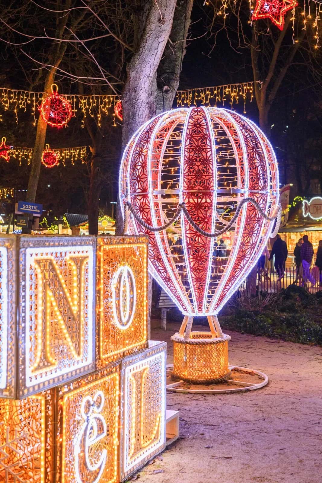Açık hava yılbaşı festivalinde kırmızı beyaz çizgili LED sıcak hava balonu ve parlak altın NOEL harf kutuları