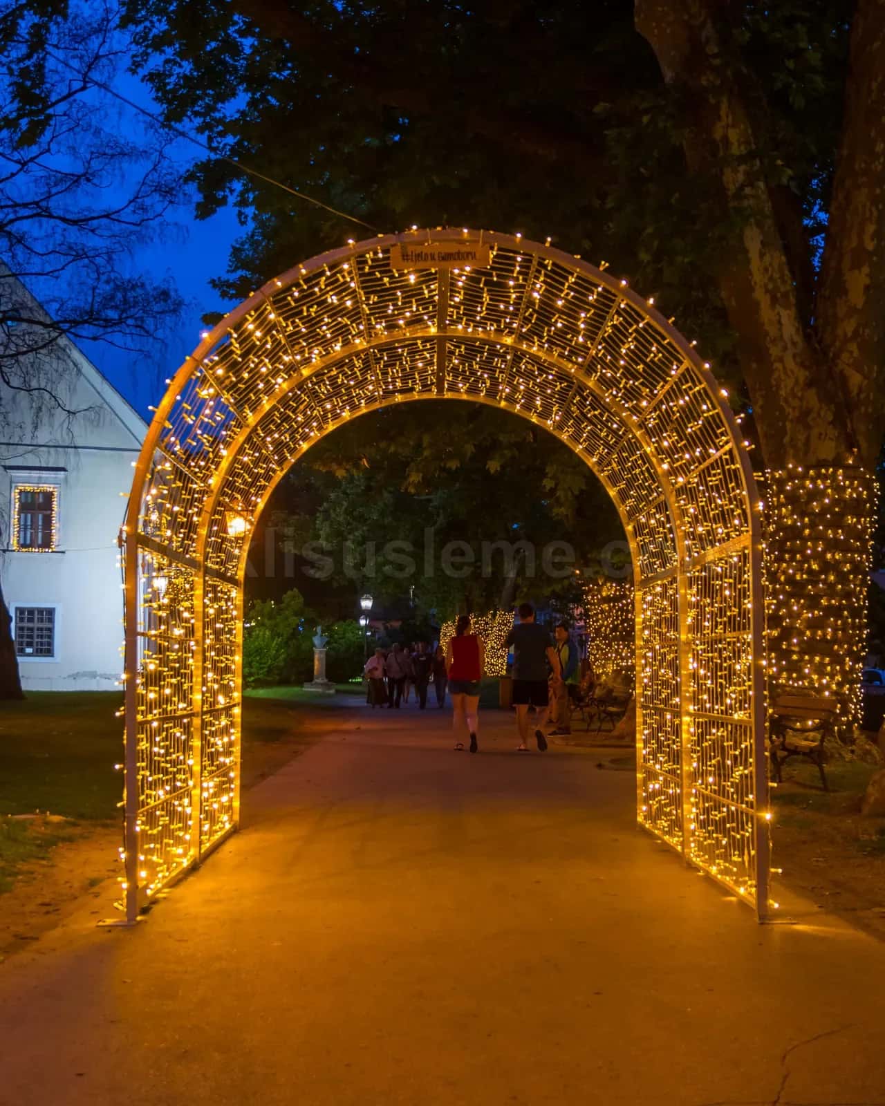 Sicak altin LED isikli kavisli metal kemer altin gece alani aydinlatiyor insanlar altindan geciyor