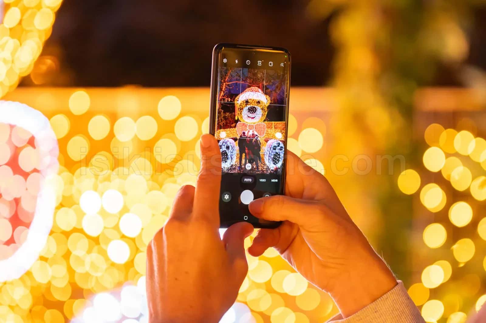 Telefon ekraninda LED Noel ayi figuru gorunurken arkada sari bokeh LED susleme parcaliyor