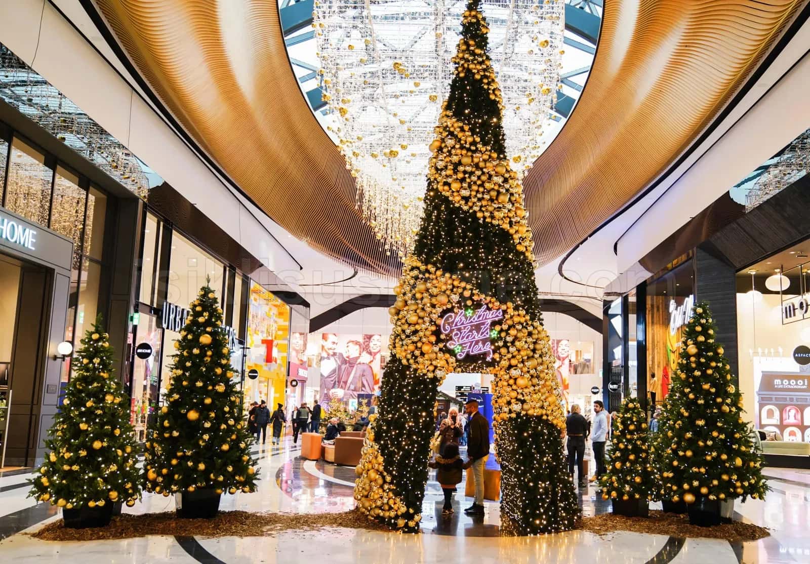Luks AVM koridorunda altin kure ve LED dizisiyle suslu dev yilbasi agaci ile etrafindaki kucuk agaclar ve alti neon tabela