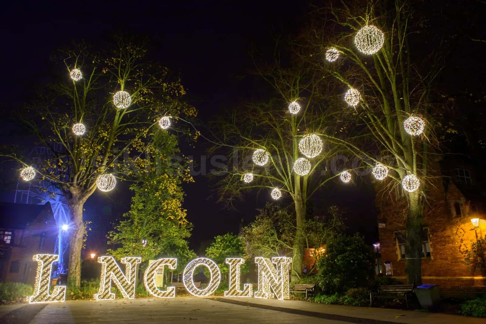 Gece meydanda agac dallarına asili sicak beyaz LED küreler ve isikli Lincoln yazisi