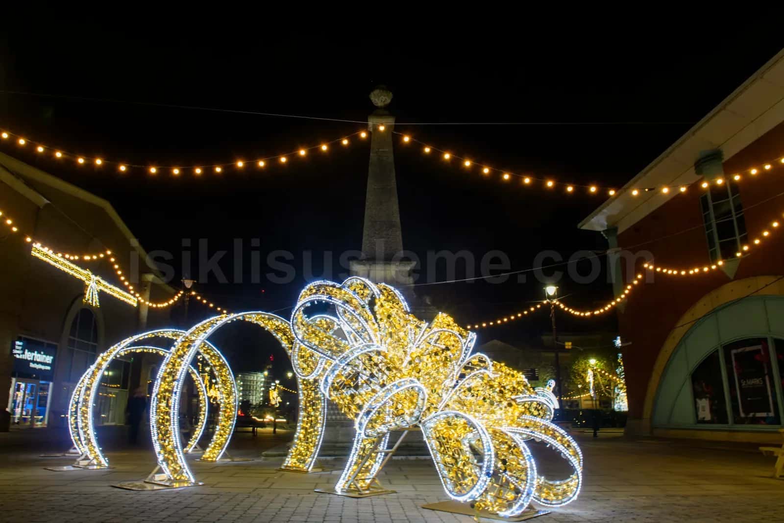 Gece aydinlatilmis meydanda yay ve cicek formlu buyuk LED figur susleme