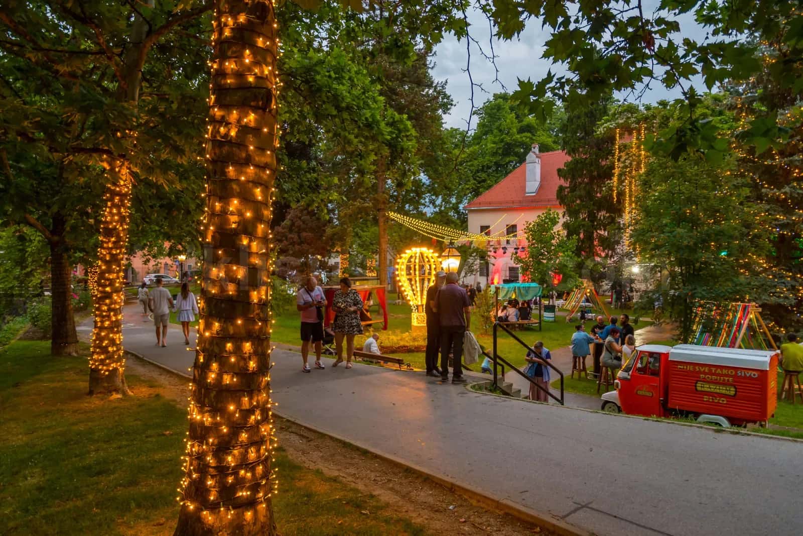 Agac gövdelerine sarili sicak sari LED zincirlerle aydinlatilmis halkın gezip eglendigi park alani
