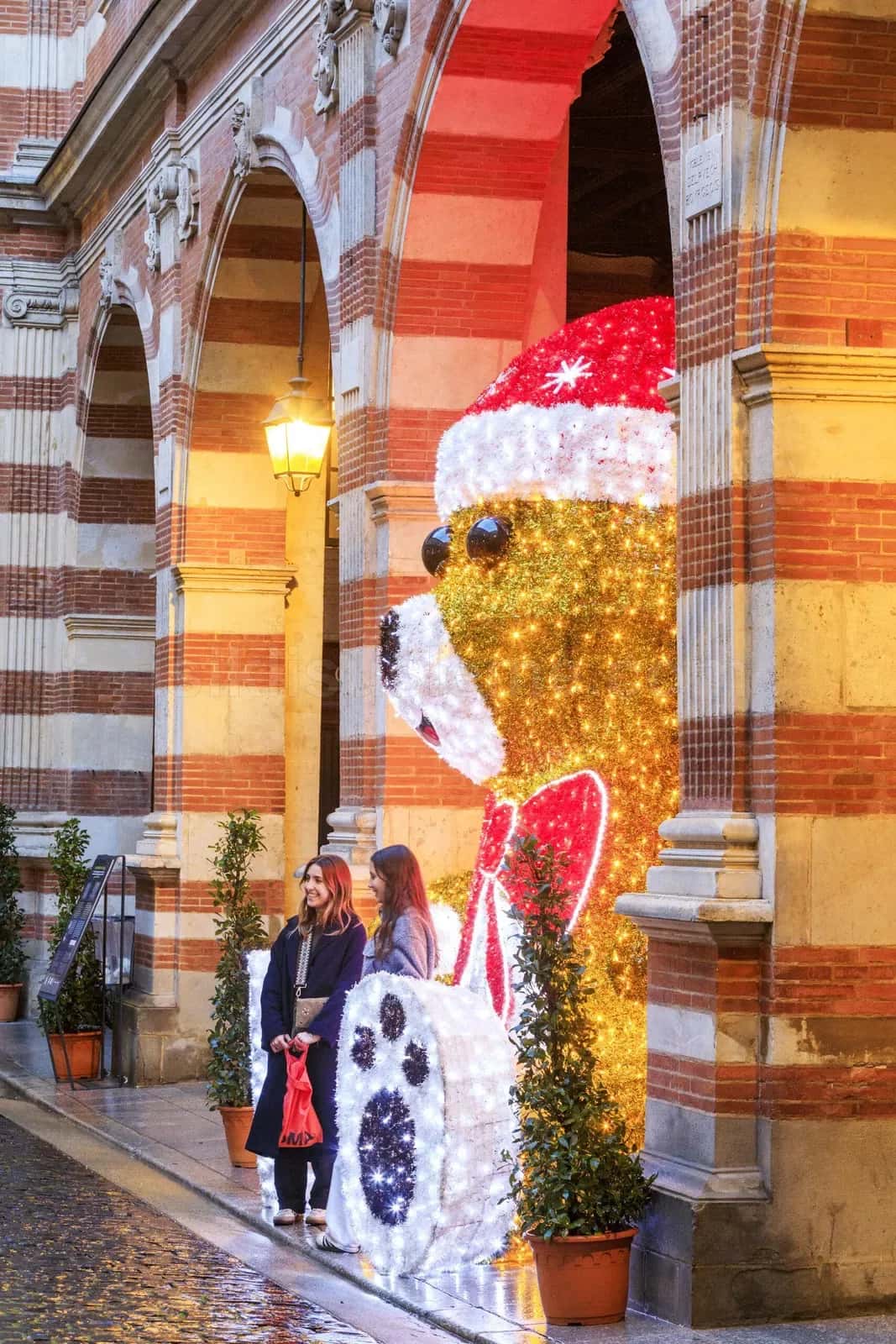Kirmizi beyaz LED ile kapli dev noel ayisi figurunun yaninda duran iki kadin tarihi tas binada