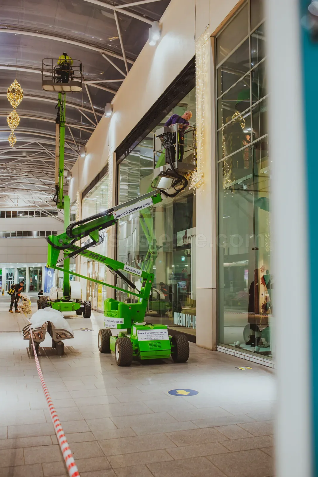 AVM koridorunda yesil platform arac ile cam cepheye LED susleme montaji yapan isci ekibi
