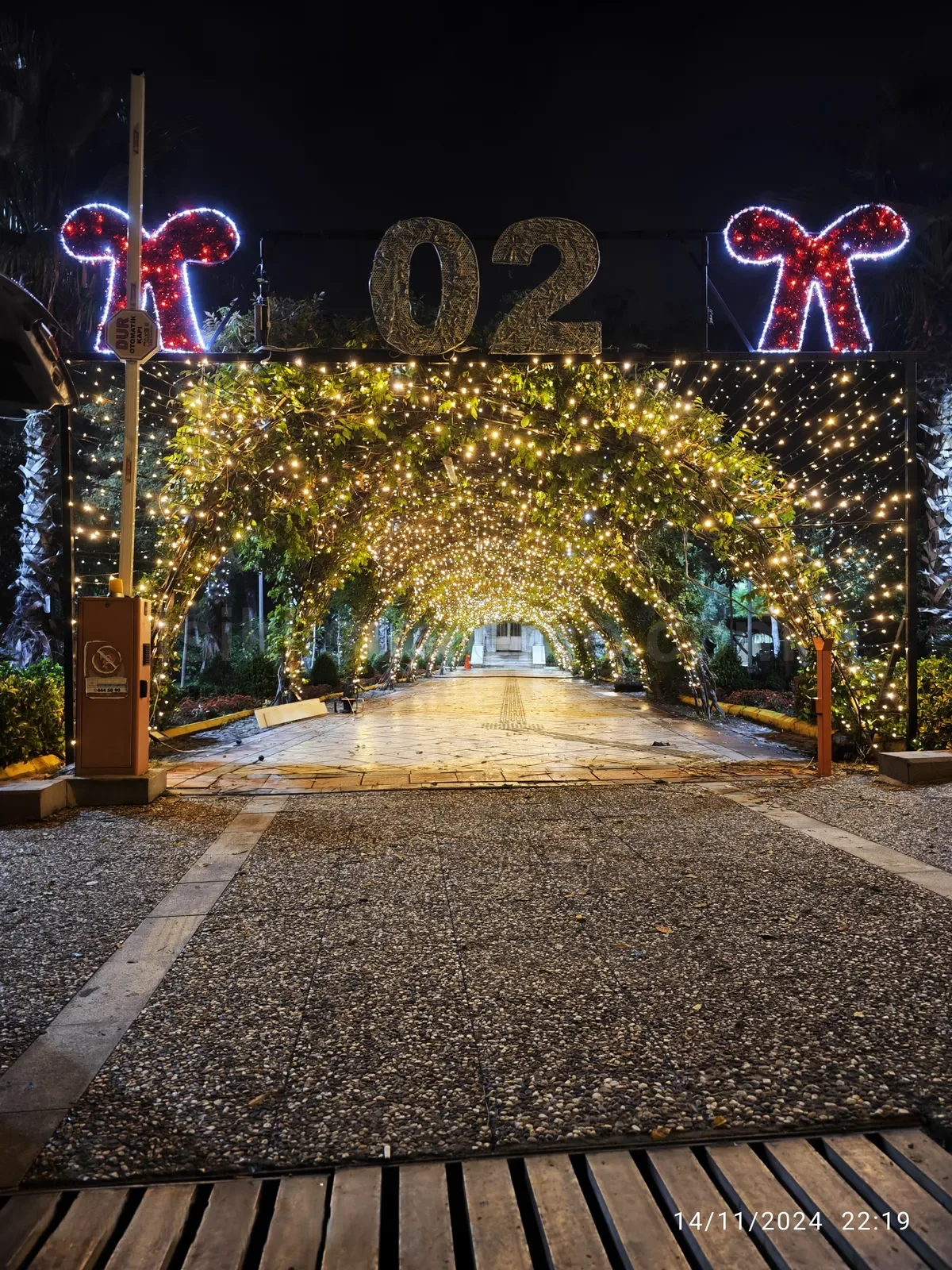 Bahce girisinde sicak beyaz peri isigi ile olusturulmus yesil tup tunel ve kirmizi fiyonk led motifler