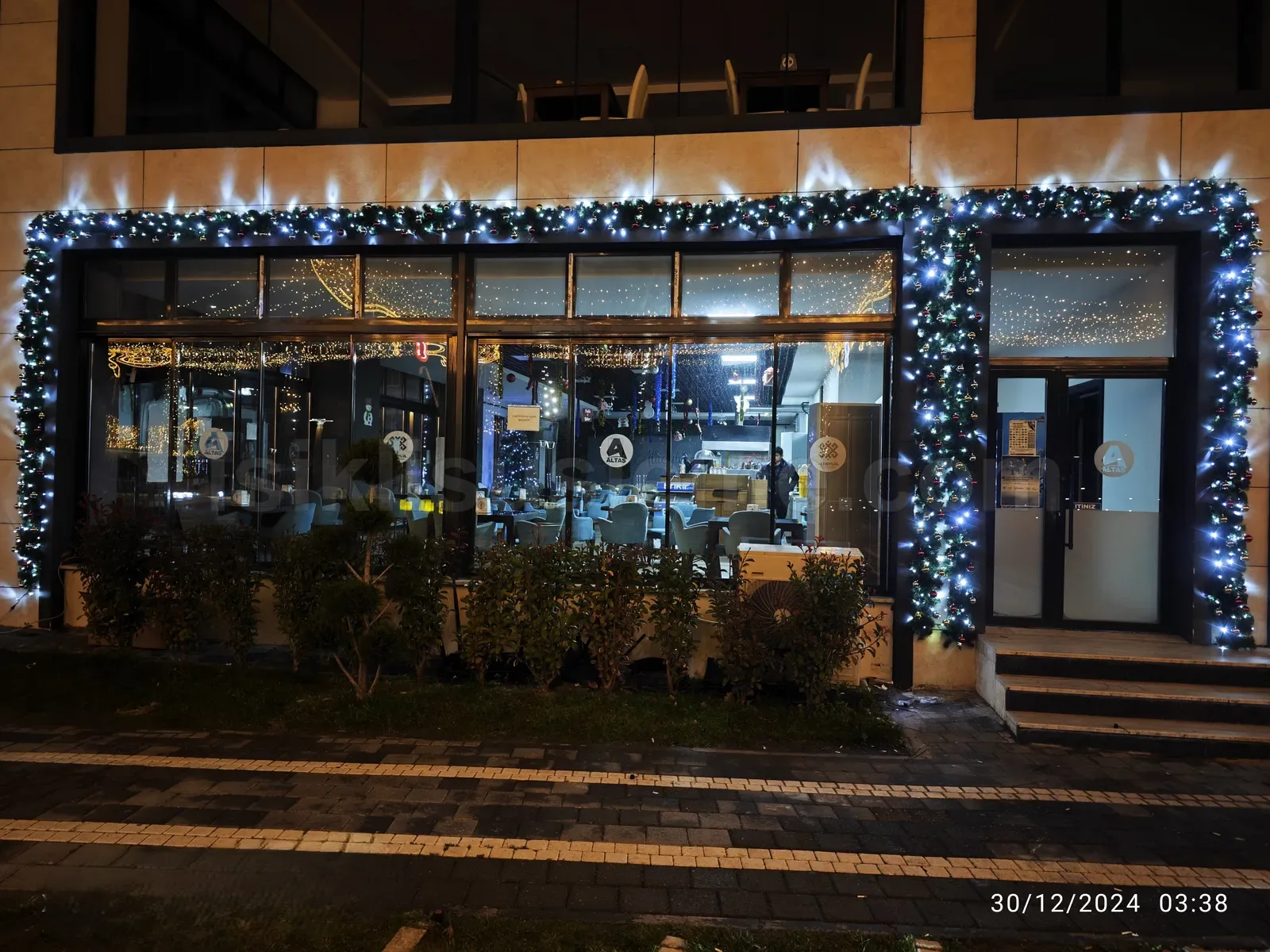 Gece kafe dis cephesinde buyuk cam pencere cercevesine mavi soguk beyaz LED garland susleme uygulanmis