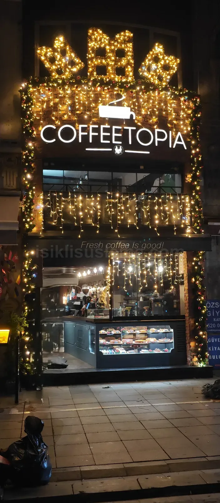 Coffeetopia kafesinin dis vitrininde sicak sari LED sarkıt ve motif suslemeyle kaplı gece cephe gorunumu