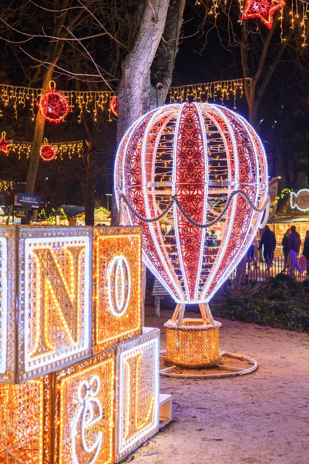 Açık hava yılbaşı festivalinde kırmızı beyaz çizgili LED sıcak hava balonu ve parlak altın NOEL harf kutuları