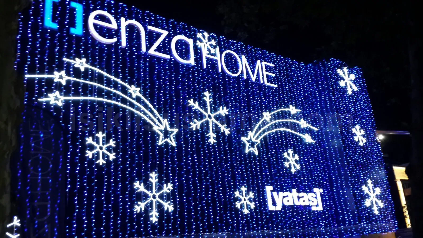 Enza Home ve Yatas markali binanin dis cephesi mavi beyaz LED perde ve kar tanesi motifleriyle kaplanmis gece gorunumu