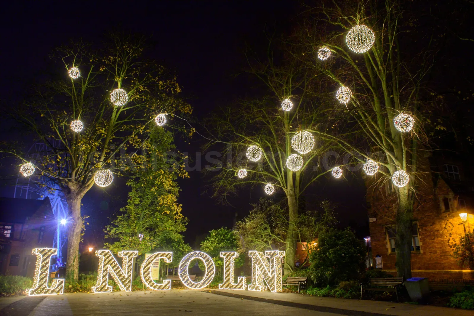 Gece meydanda agac dallarına asili sicak beyaz LED küreler ve isikli Lincoln yazisi