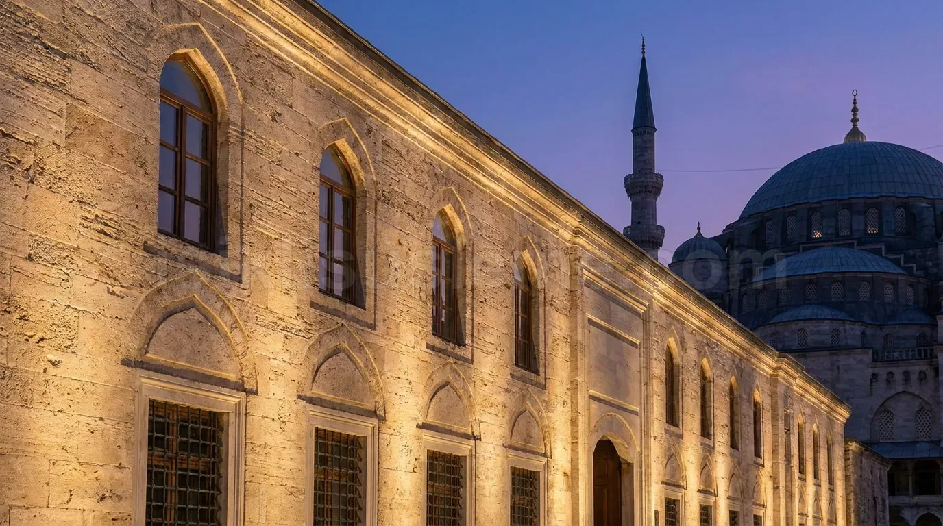Mavi saat isiginda tarihi Osmali yapisi cephesi sicak sari LED uplight ile vurgulanmis