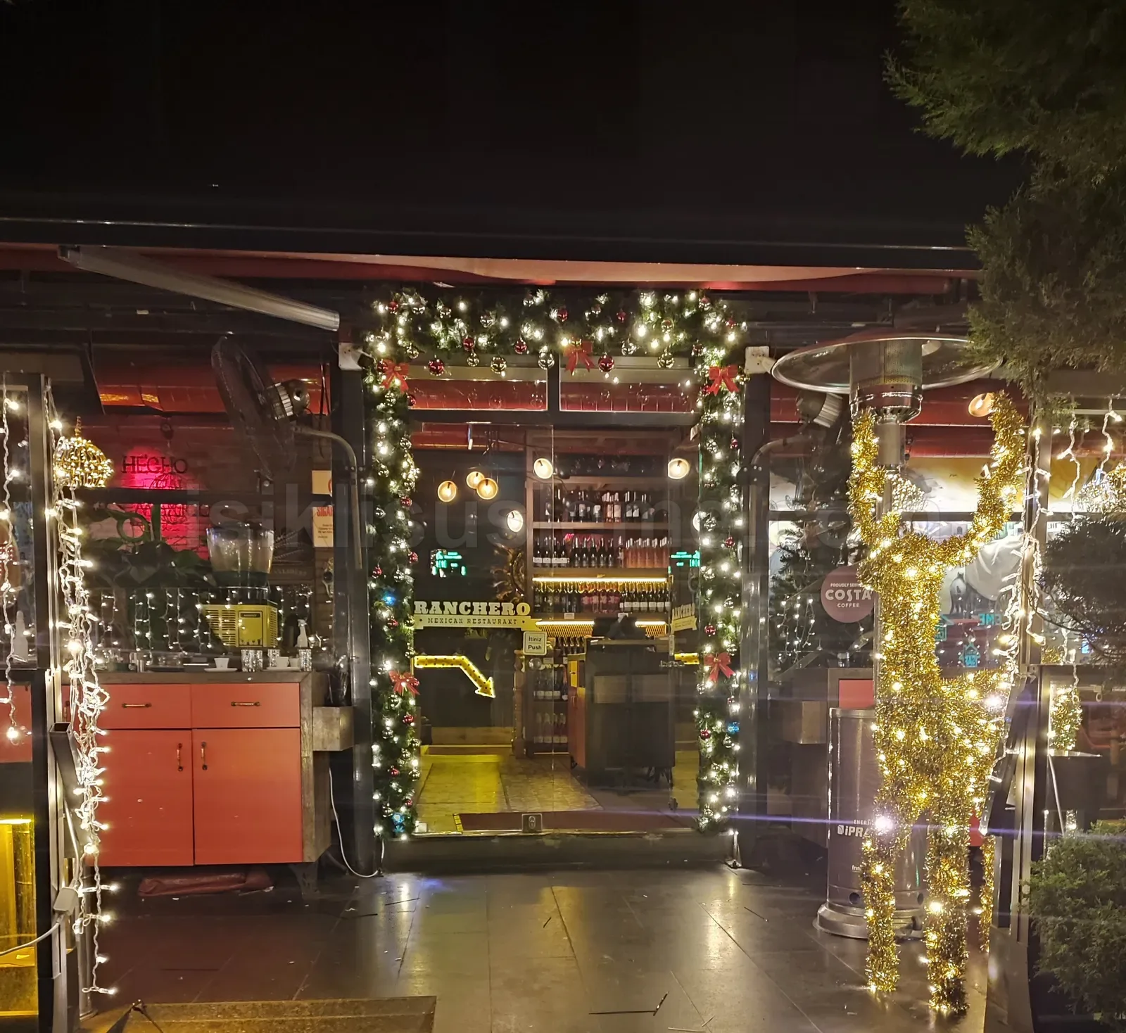 Ranchero restoraninin giris kapisi kemeri yilbasi cami altin LED zincir ve isik sarkıtlarıyla suslenmiş gece gorunumu