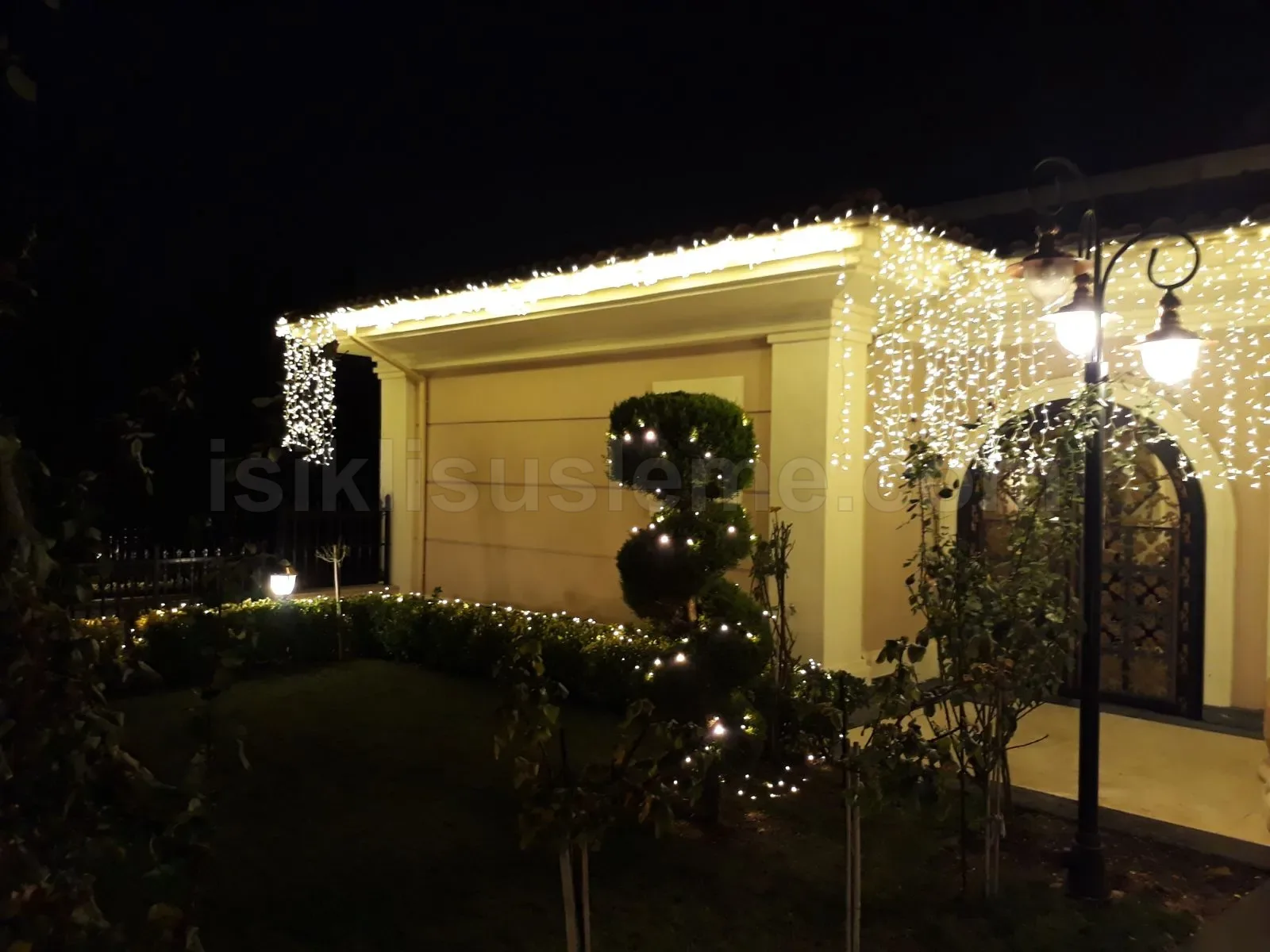 Villa bahce cephesinde sacak perde LED ve budanmis topiary agac uzerine sicak beyaz peri isigi