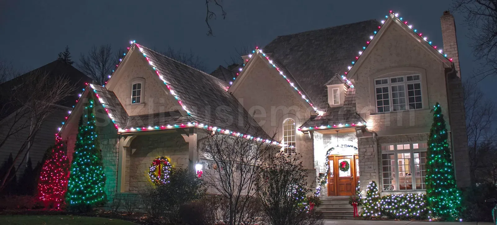 Gece kirmizi beyaz ve yesil LED isiklar ile suslenmus villa cephesi ve onundeki agaclar