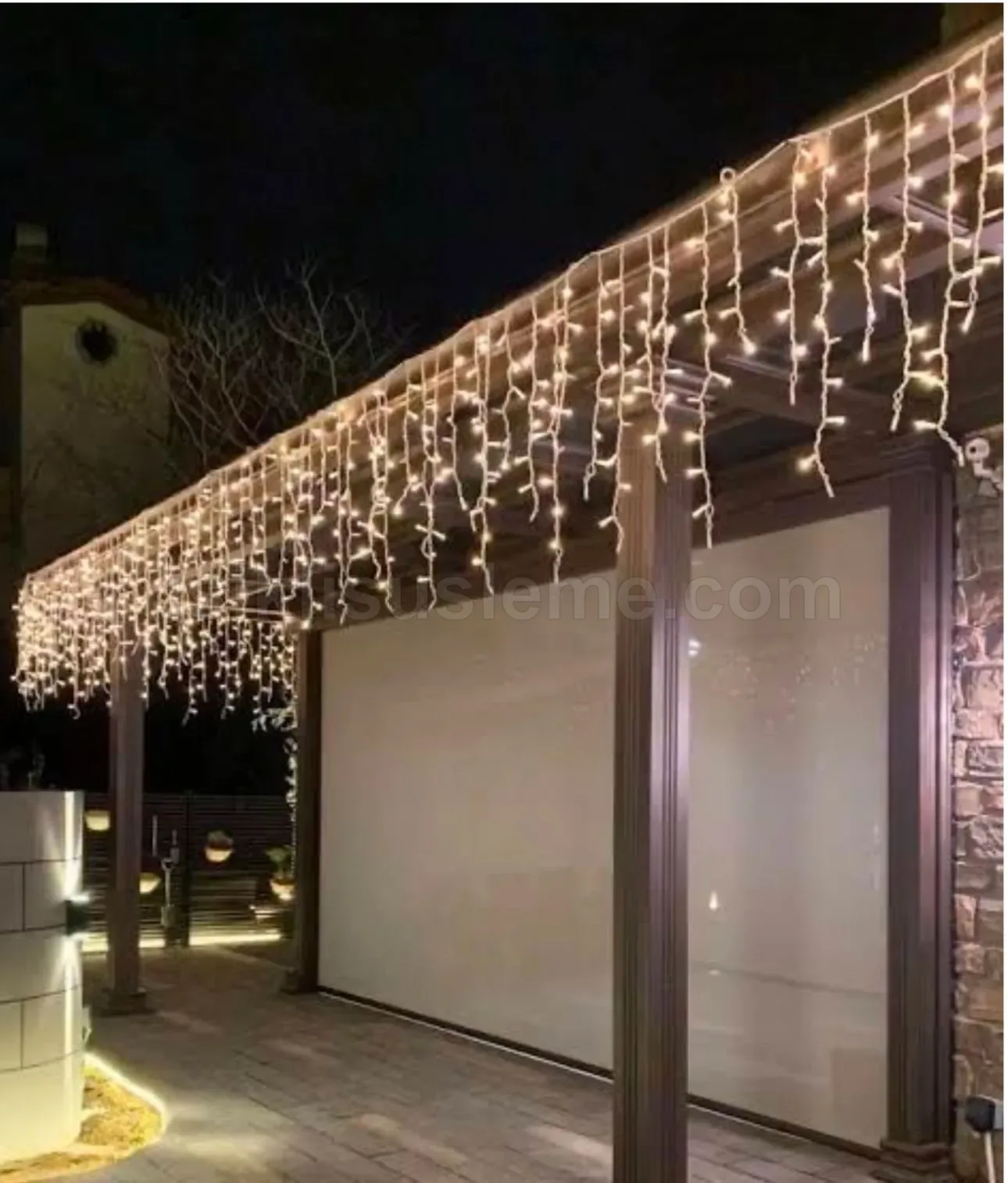Ahsap pergolali villa terasinda sarimsi sicak beyaz sarkac LED perdenin asin altindaki modern dis mekan gece gorunumu