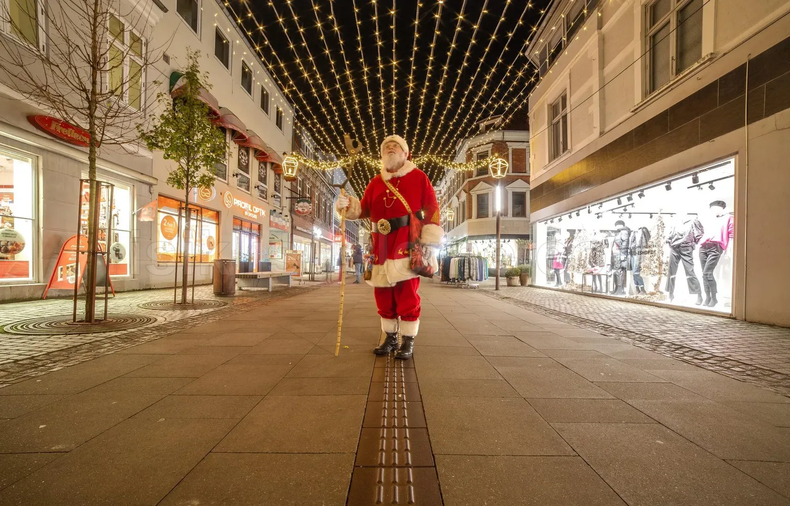Yaya alisveris caddesinde tavan boyunca geren sari LED perde altinda Noel Baba kostumlu kisi